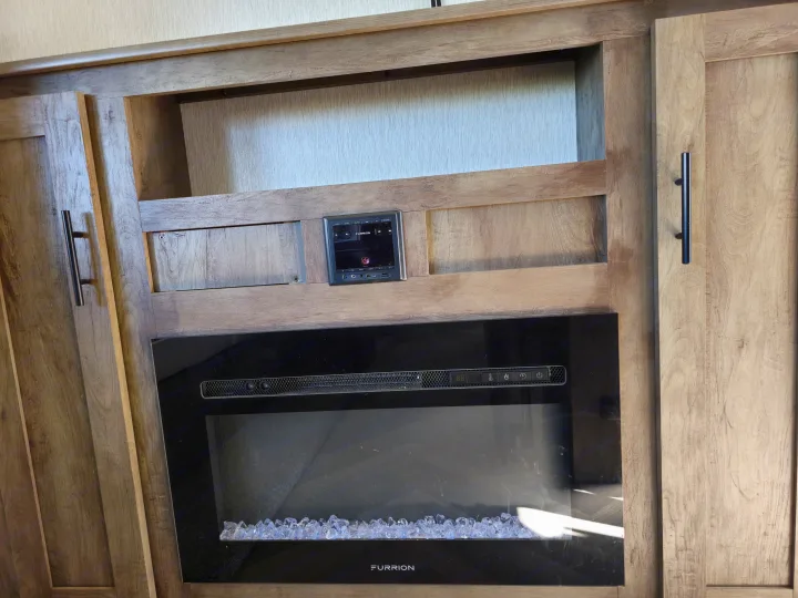 RV rental interior featuring a modern Furrion electric fireplace and entertainment system integrated into light wood cabinetry.. Forest River Wildwood X-Lite 2022