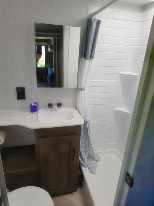 Clean RV rental bathroom with a vanity, sink, toilet, and compact shower featuring a white tile-patterned surround.. Forest River Wildwood X-Lite 2022