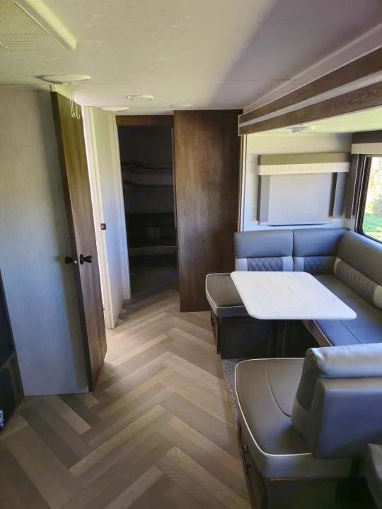 Spacious RV rental interior with a modern gray dinette, white table, and herringbone flooring, leading to a bunk area.. Forest River Wildwood X-Lite 2022