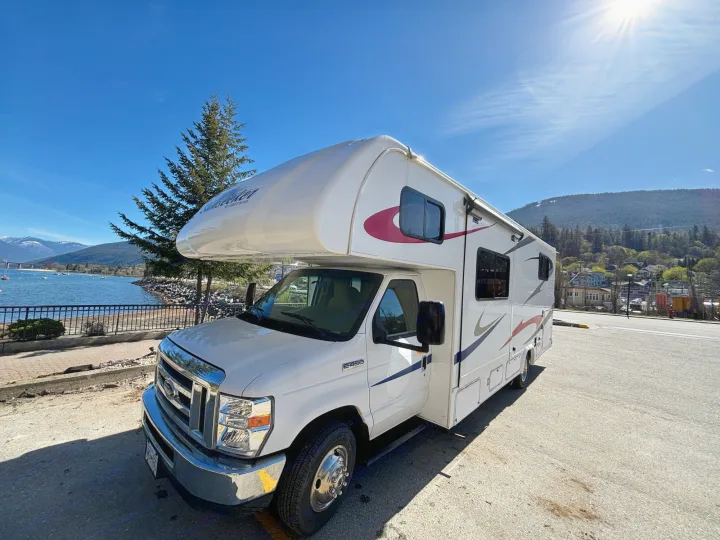 This white RV rental is parked by a scenic lake on a sunny day, with mountains in the background.. Forest River Sunseeker 2018