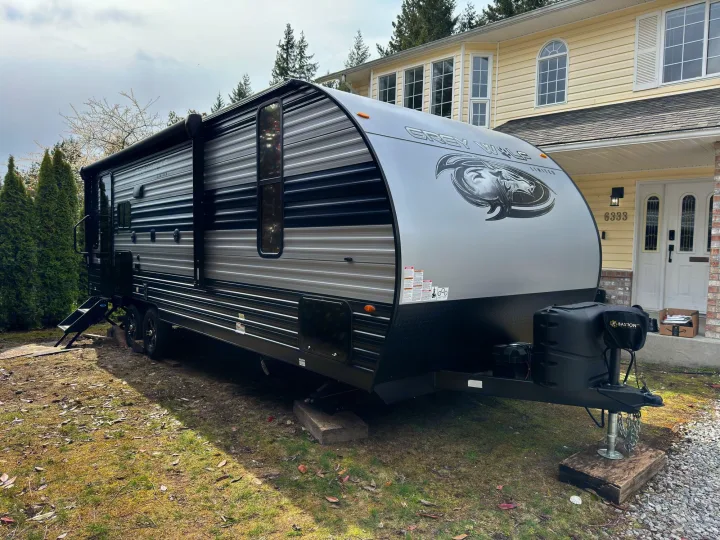 This large Grey Wolf travel trailer, an ideal RV rental, is parked in a residential yard next to a yellow house.. Greywolf 23MK 2022