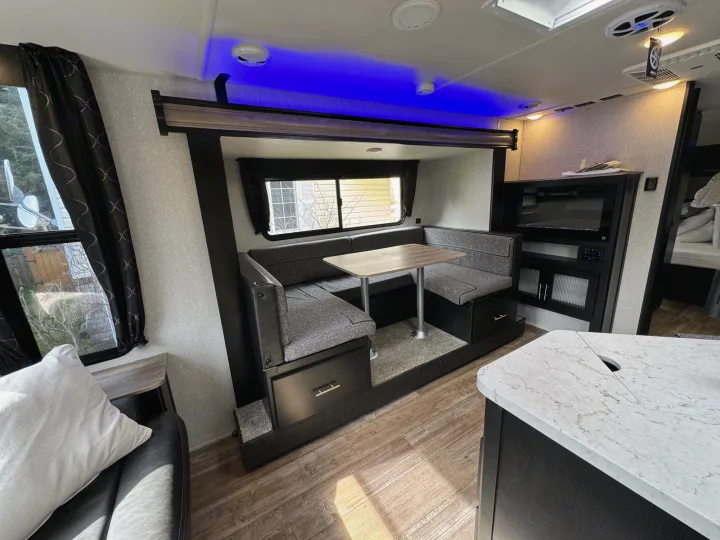 Modern RV rental interior with cozy dinette, ambient blue lighting, TV, & kitchen. Ideal for travel comfort.. Greywolf 23MK 2022