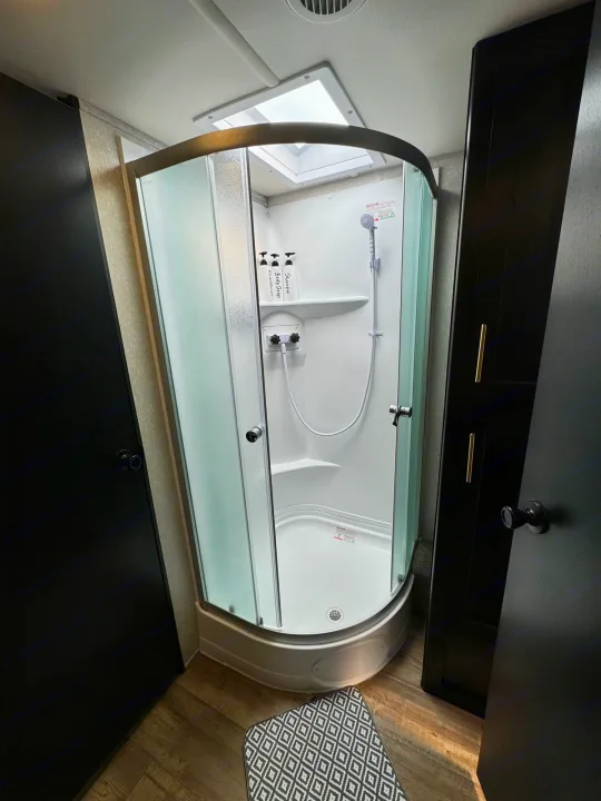Interior of an RV rental bathroom, showcasing a compact corner shower with frosted glass doors, shower head, and amenities.. Greywolf 23MK 2022