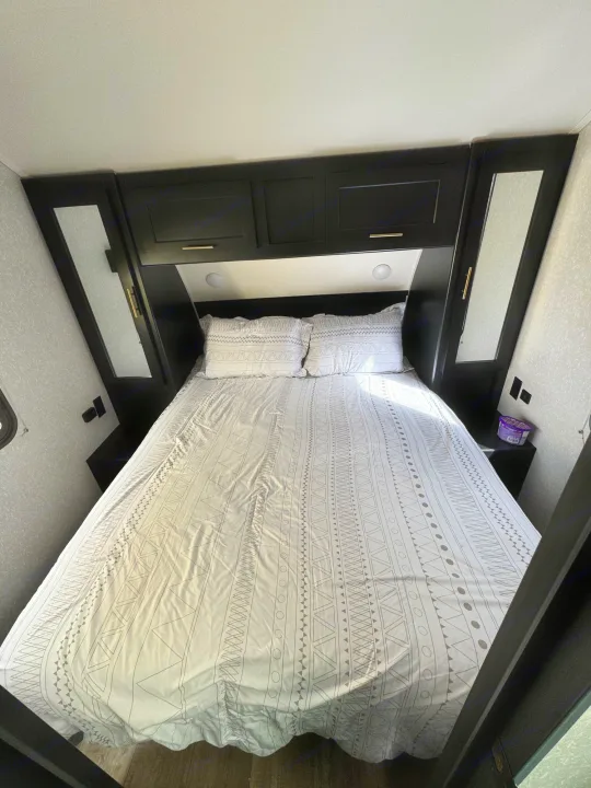 RV rental bedroom featuring a patterned bed, black overhead storage, and mirrored wardrobe cabinets. Bright and functional.. Greywolf 23MK 2022