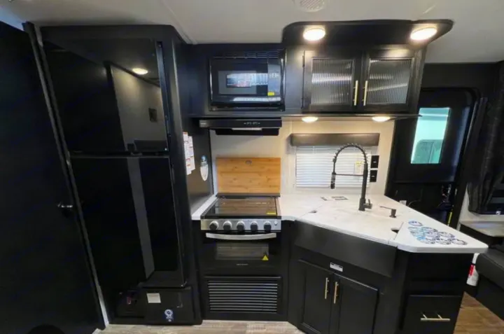 Modern RV rental kitchen featuring black appliances, white counters, and sleek design with ample storage.. Greywolf 23MK 2022
