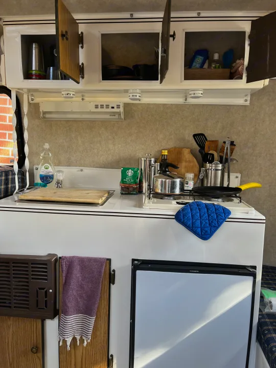 Compact RV rental kitchen with open cabinets, a stove, Dometic fridge, and cooking essentials ready.. Scamp Scamp Trailer 2004