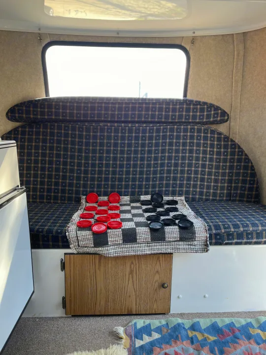 Inside a cozy rv rental: plaid seating, bright window, and a checkers game laid out on a mat.. Scamp Scamp Trailer 2004