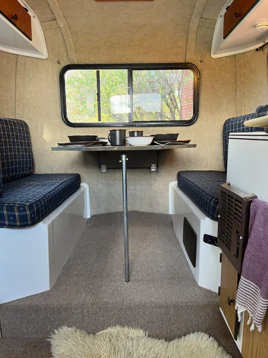 Compact RV rental interior: cozy dining area with plaid cushions, table, and window views.. Scamp Scamp Trailer 2004