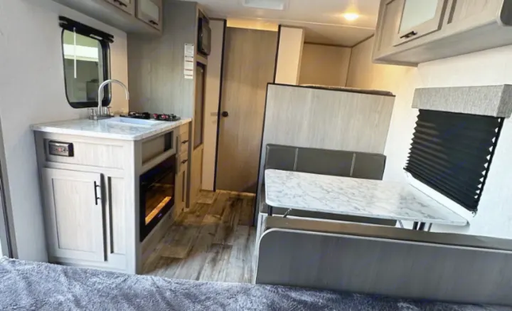 Interior of an RV rental showing a functional kitchenette with sink and stovetop, plus a comfortable dinette. Bright camper living space.. Coleman Lantern 17b 2024
