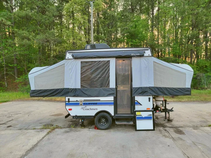 A white and gray Clipper Coachmen pop-up RV rental is fully set up on a paved lot, ready for your camping adventures.. Forest River Coachmen LS 2020