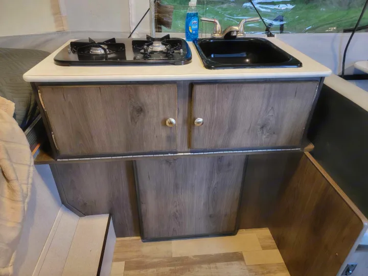Compact RV rental kitchen features a two-burner stove, sink, and wood-look cabinets. Perfect for cooking on the go.. Forest River Coachmen LS 2020