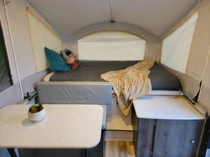 Cozy pop-up RV rental interior with bed, table, and seating. Perfect for comfortable glamping adventures.. Forest River Coachmen LS 2020