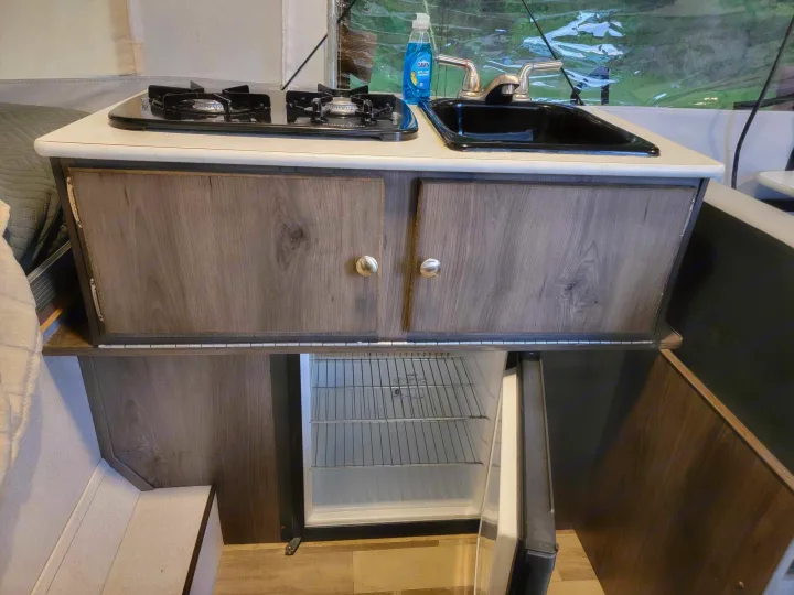 Compact RV rental kitchen with a gas stove, sink, cabinets, and an open mini-fridge, ideal for travel.. Forest River Coachmen LS 2020