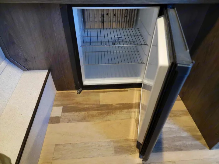 An open Dometic mini-fridge with wire shelves inside an RV rental's compact kitchen area.. Forest River Coachmen LS 2020