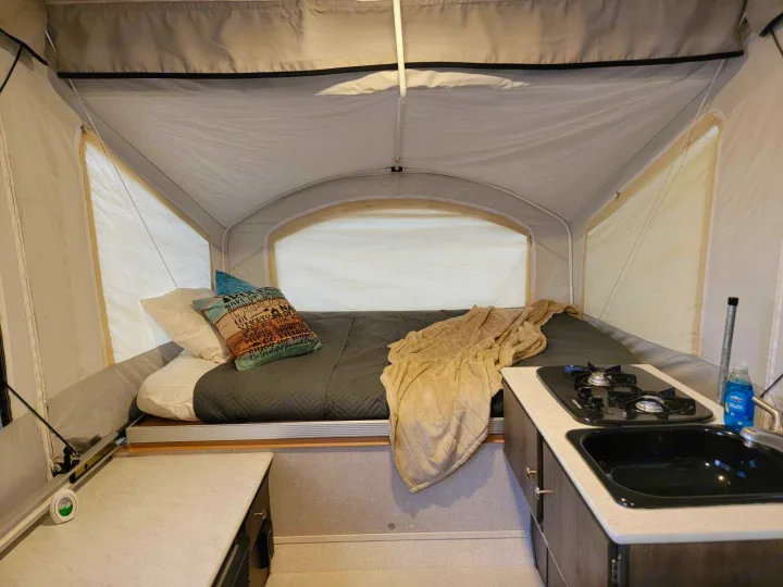 Cozy RV rental pop-up camper interior: features a comfortable bed, functional kitchen with stove, and sink.. Forest River Coachmen LS 2020