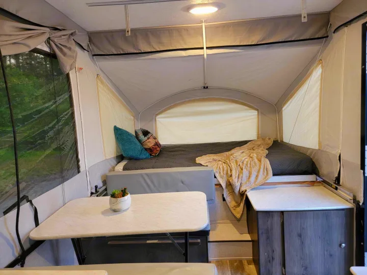 The inviting interior of a pop-up RV rental, featuring a cozy bed, dining table with a plant, and storage cabinets.. Forest River Coachmen LS 2020