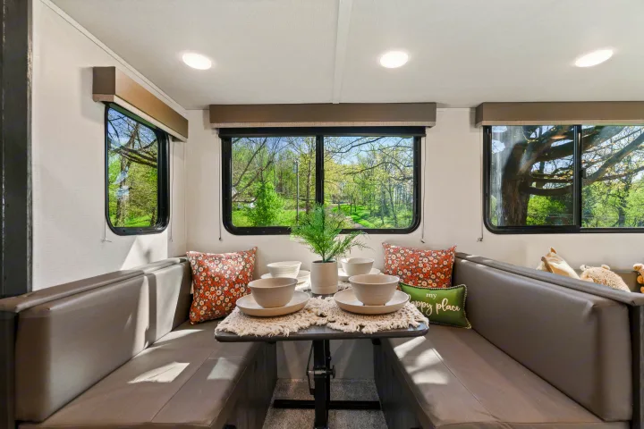 Cozy RV rental dinette with comfortable seating, a set table, and scenic views from the windows. Perfect for dining & relaxing.. Keystone RV Hideout 2022
