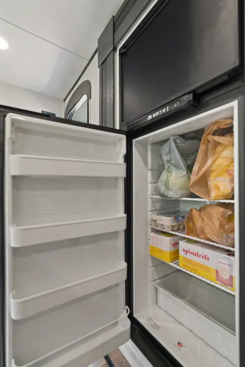 Open refrigerator in an RV rental, stocked with groceries: eggs, produce bags, and Spindrift sparkling water. Perfect for road trips.. Keystone RV Hideout 2022
