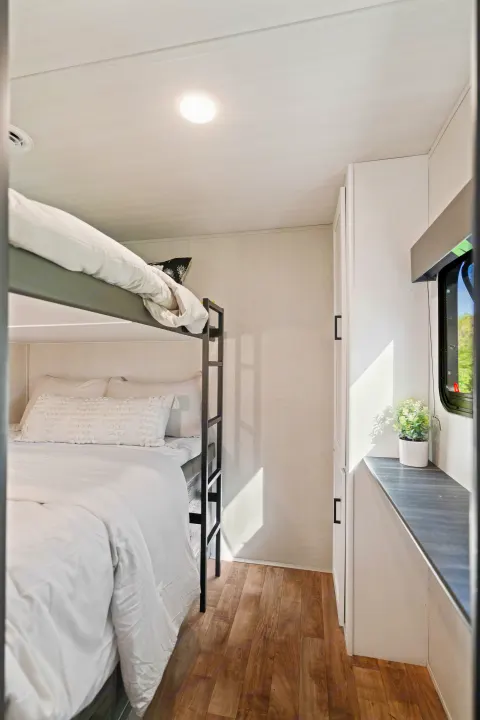 Cozy RV rental interior featuring comfortable bunk beds with white bedding, bright natural light, and ample storage.. Keystone RV Hideout 2022