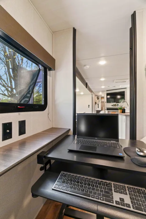 Comfortable RV rental with a dedicated mobile office, featuring a laptop, keyboard, and window view. Ideal for travel and work.. Keystone RV Hideout 2022