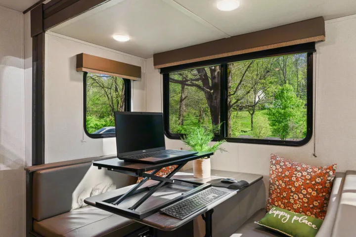 RV rental interior with a comfortable, well-lit mobile workspace, featuring a laptop on a desk converter by scenic windows.. Keystone RV Hideout 2022