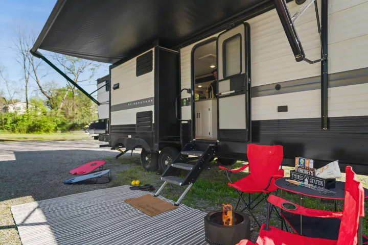 An rv rental is set up with an extended awning, chairs, fire pit, s'mores station, & cornhole for outdoor fun.. Keystone RV Hideout 2022