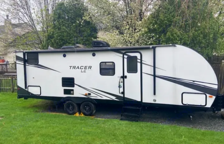 A white Tracer LE travel trailer with black accents, parked on a grassy lot. Perfect for an RV rental adventure.. Forest River Tracer LE 2020