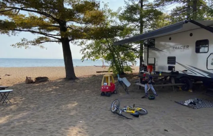 Family fun at an RV rental beach site: a travel trailer parked by the water, with children's toys and a picnic area.. Forest River Tracer LE 2020