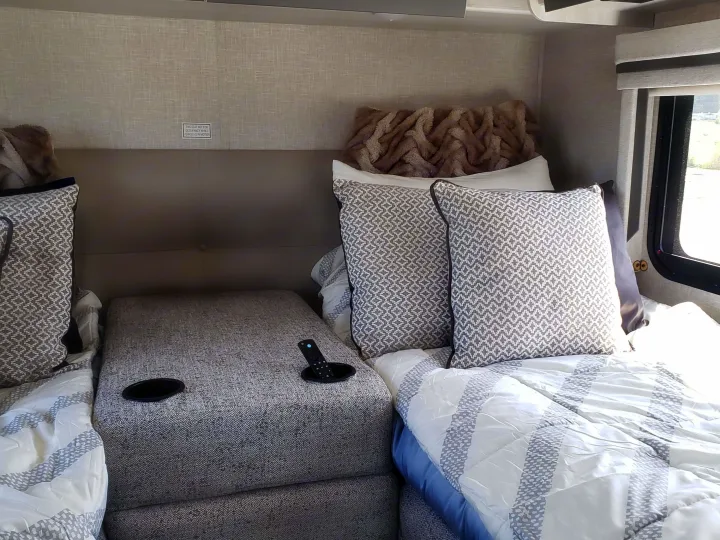 Inside an RV rental: Relaxing twin beds with patterned pillows, white comforters, and a central console with cup holders.. Thor Compass 2024
