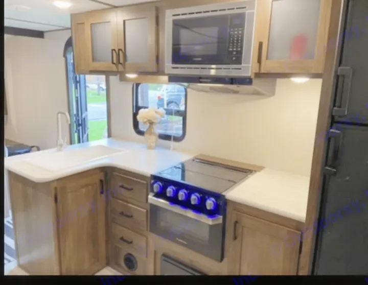 This RV rental kitchen features a modern sink, stove, microwave, wood cabinets, and light countertops.. Forest River Tracer LE 2020