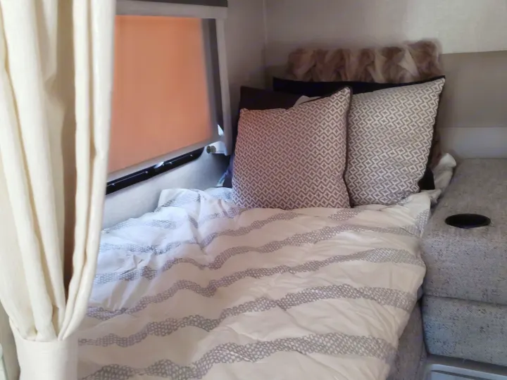 Cozy RV rental bedroom featuring white and grey striped bedding, plush pillows, and a window, ideal for comfortable travel.. Thor Compass 2024