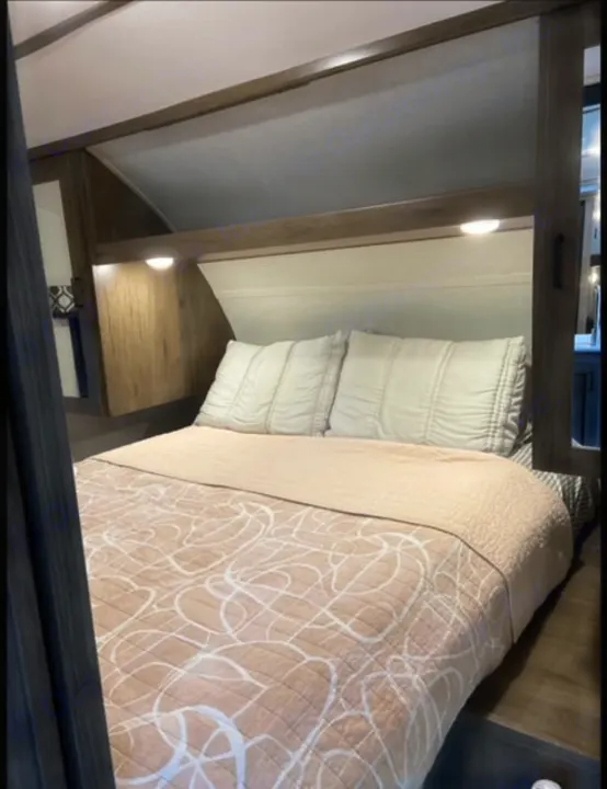 Cozy RV rental bedroom featuring a comfortable bed with light bedding, wooden headboard, and built-in overhead lighting.. Forest River Tracer LE 2020