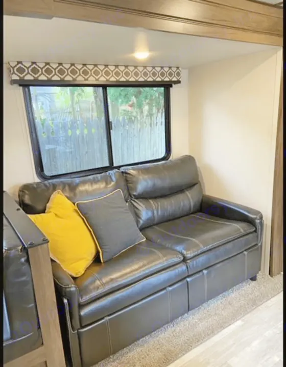 RV rental living area: comfy black leather couch with yellow & grey pillows, decorative window, and outdoor view.. Forest River Tracer LE 2020