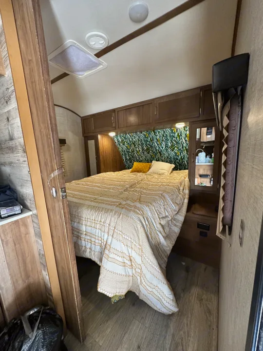 Inside an RV rental: a cozy bedroom featuring an elegant bed, overhead cabinets, and a vibrant leaf accent wall.. Gulf Stream Envision 2020