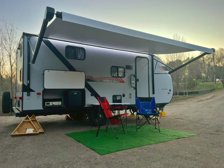 Perfect RV rental ready for adventure! This travel trailer features an illuminated awning, outdoor kitchen, and cozy campsite setup.. Wildwood FSX 2021