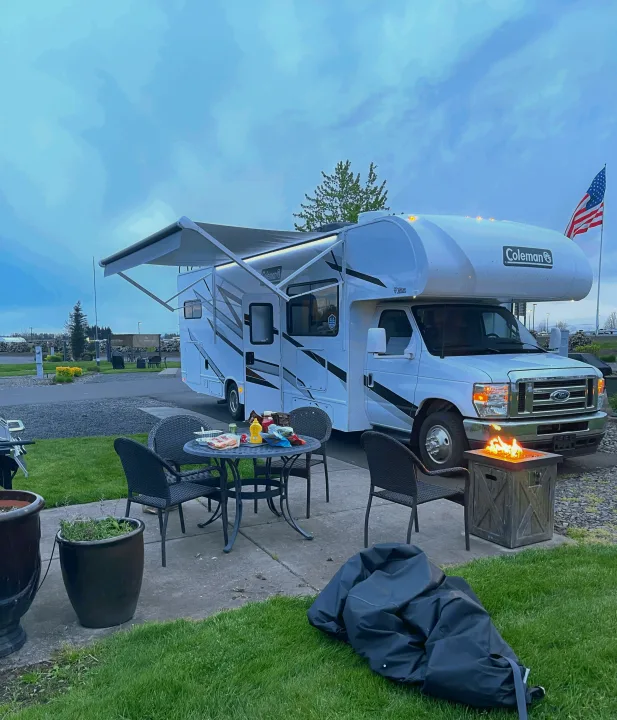 RV rental at a vibrant campsite: awning extended, fire pit glowing, and outdoor dining ready for an evening.. Thor Coleman 2024