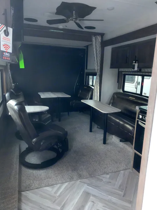 Spacious RV rental interior: brown recliners, tables, and a sofa on gray carpet, with wood-look flooring and a ceiling fan.. Forest River Stealth 2021