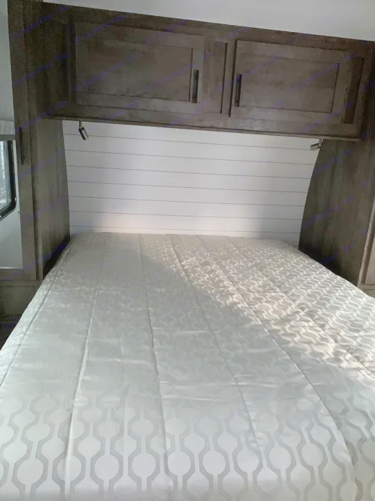 Cozy RV rental bedroom with shiplap headboard, overhead storage, reading lights, and patterned comforter.. Forest River Stealth 2021