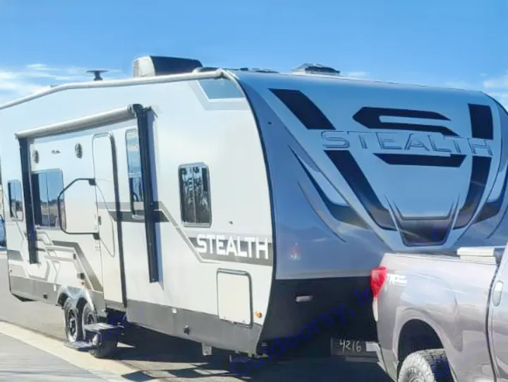 A large gray Stealth travel trailer/toy hauler, a great rv rental option, is shown hitched to a pickup truck.. Forest River Stealth 2021