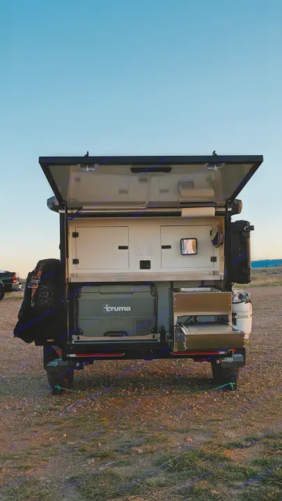 Rear view of an open overland camper trailer's outdoor kitchen, with a Truma fridge and pull-out stove. Consider this for your rv rental.. Boreas XT 2023