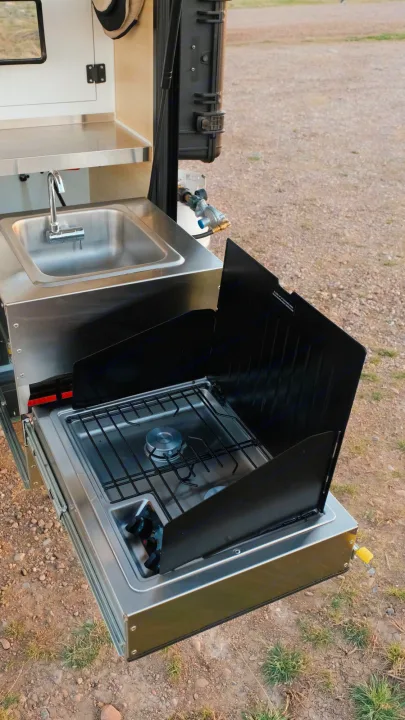 RV rental outdoor kitchen features a pull-out stainless steel sink and gas stove with wind guards for campsite cooking.. Boreas XT 2023