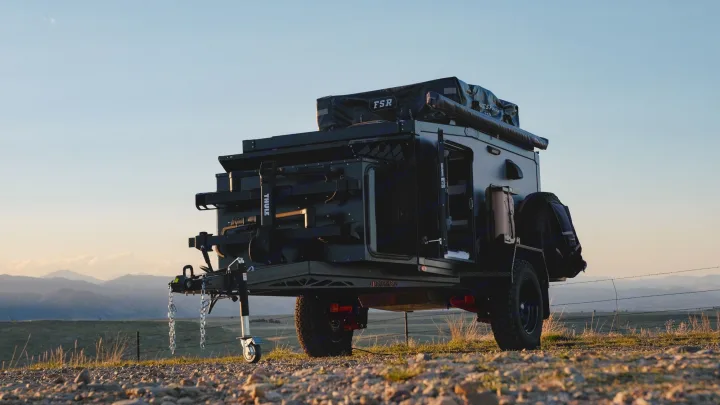 A rugged black overlanding trailer with a rooftop tent and gear, parked on a dirt path with mountains in the background. Perfect for an RV rental adventure.. Boreas XT 2023