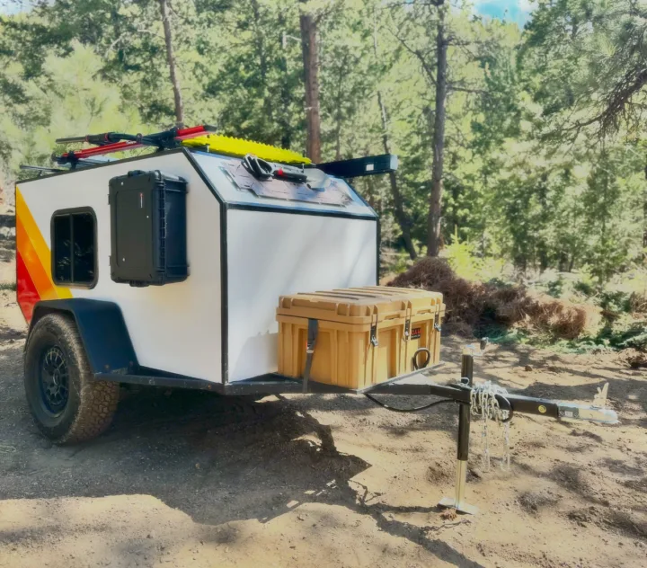 Adventure-ready overland camper trailer in a forest. Perfect for your next RV rental and off-road camping trip.. Custom Retro 2023