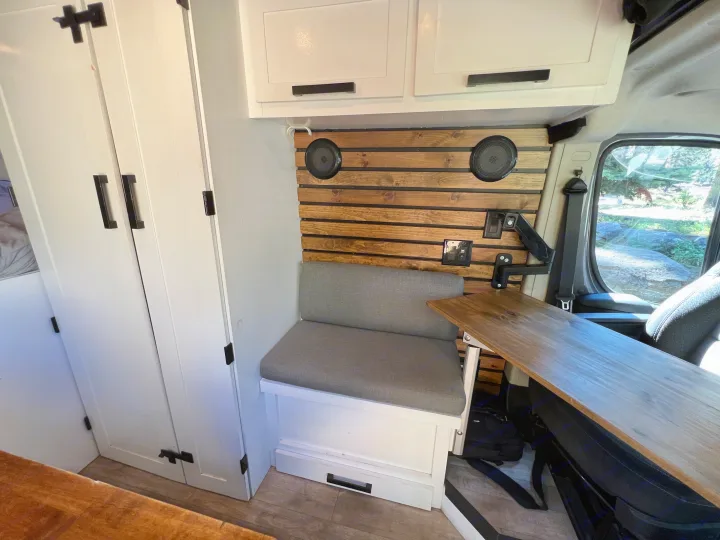 Inside an RV rental: white cabinets, wooden wall, gray bench, and an adjustable table, creating a functional travel space.. Dodge Sprinter Van 2019