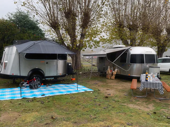 Two silver travel trailers, including a classic Airstream, are set up at a misty campground. A perfect RV rental getaway scene.. Airstream Basecamp 2022