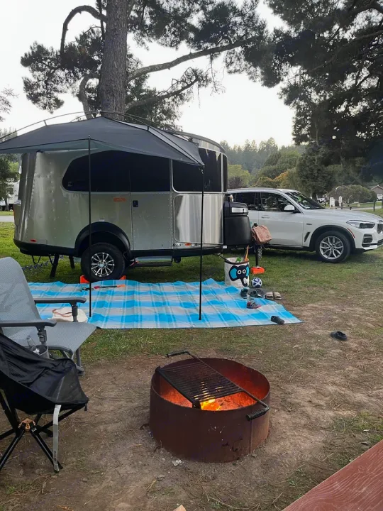 Camping with a sleek RV rental & SUV. Fire pit, mat, & chairs ready for evening relaxation at the campground.. Airstream Basecamp 2022