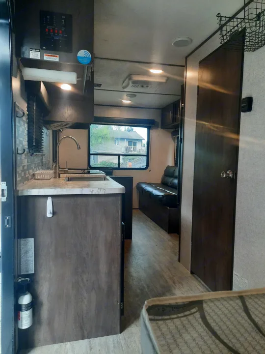 RV rental interior: Modern kitchen with stainless sink & backsplash, plus a comfy sofa in the living area.. Dutchmen Aspen 2020