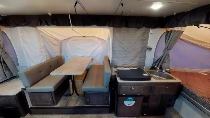 Efficient pop-up RV rental interior: dinette, compact kitchen with sink, and cozy bed. Ready for camping trips.. Forest River Rockwood ESP 2023