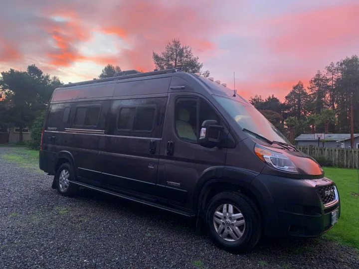 Dark gray Winnebago Travato camper van parked on gravel under a beautiful pink sunset. Ideal for your next rv rental.. Winnebago Travato 2022