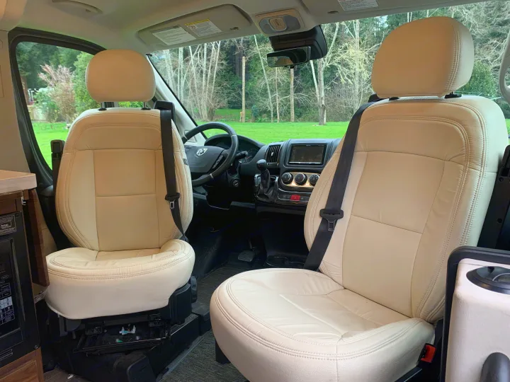 Spacious rv rental interior featuring cream swivel seats, driver's cockpit, and scenic views. Ideal for comfortable travel.. Winnebago Travato 2022